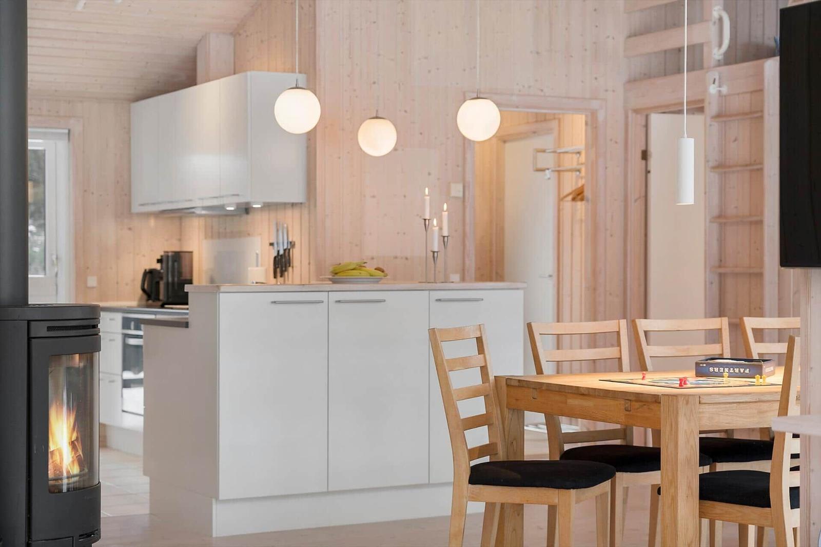 Kitchen with dining table, wooden walls, and wood-burning stove. Modern built-in kitchen with wooden chairs.
