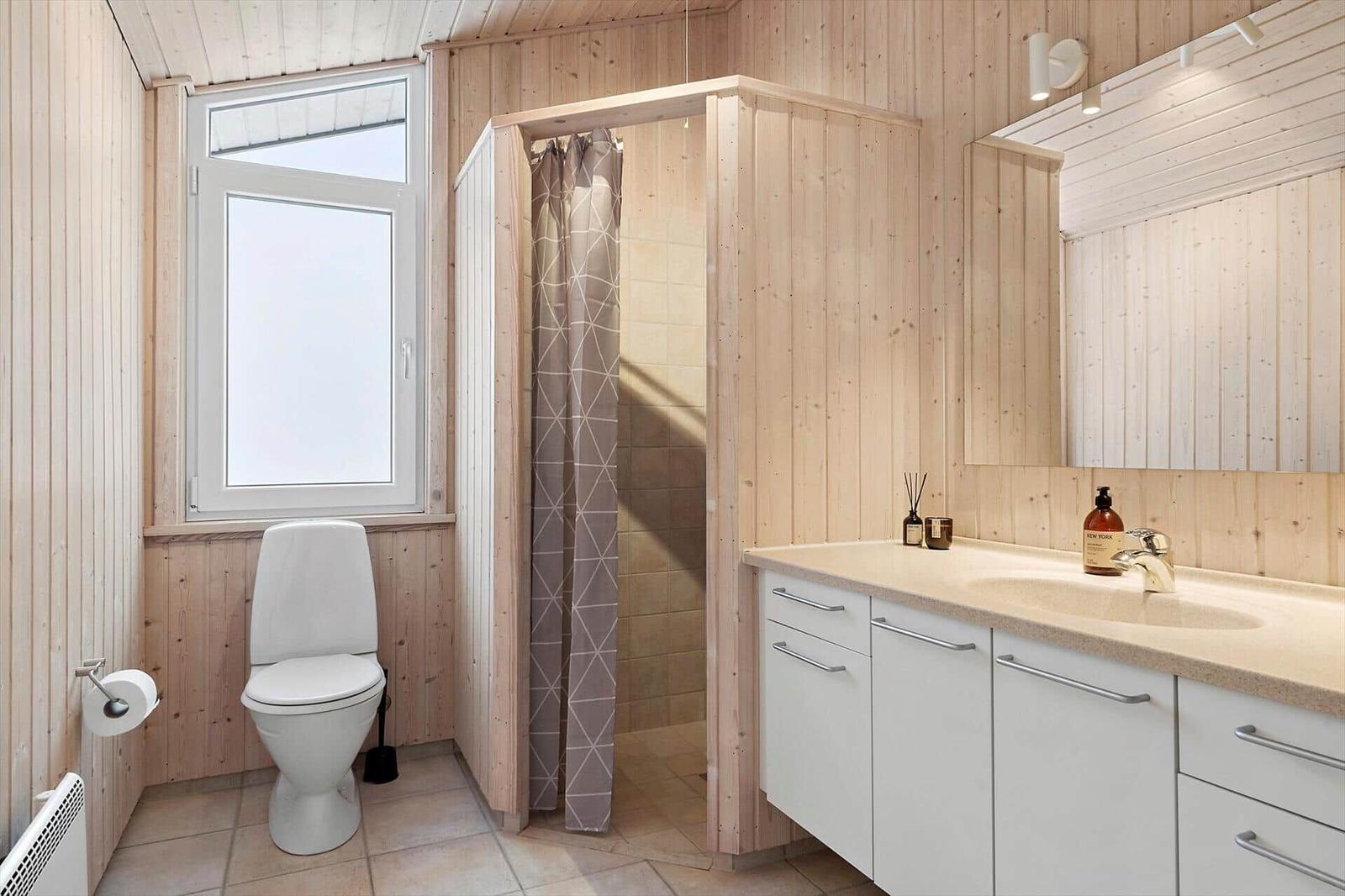 Bathroom with toilet, shower, and sink. Wooden walls and window.
