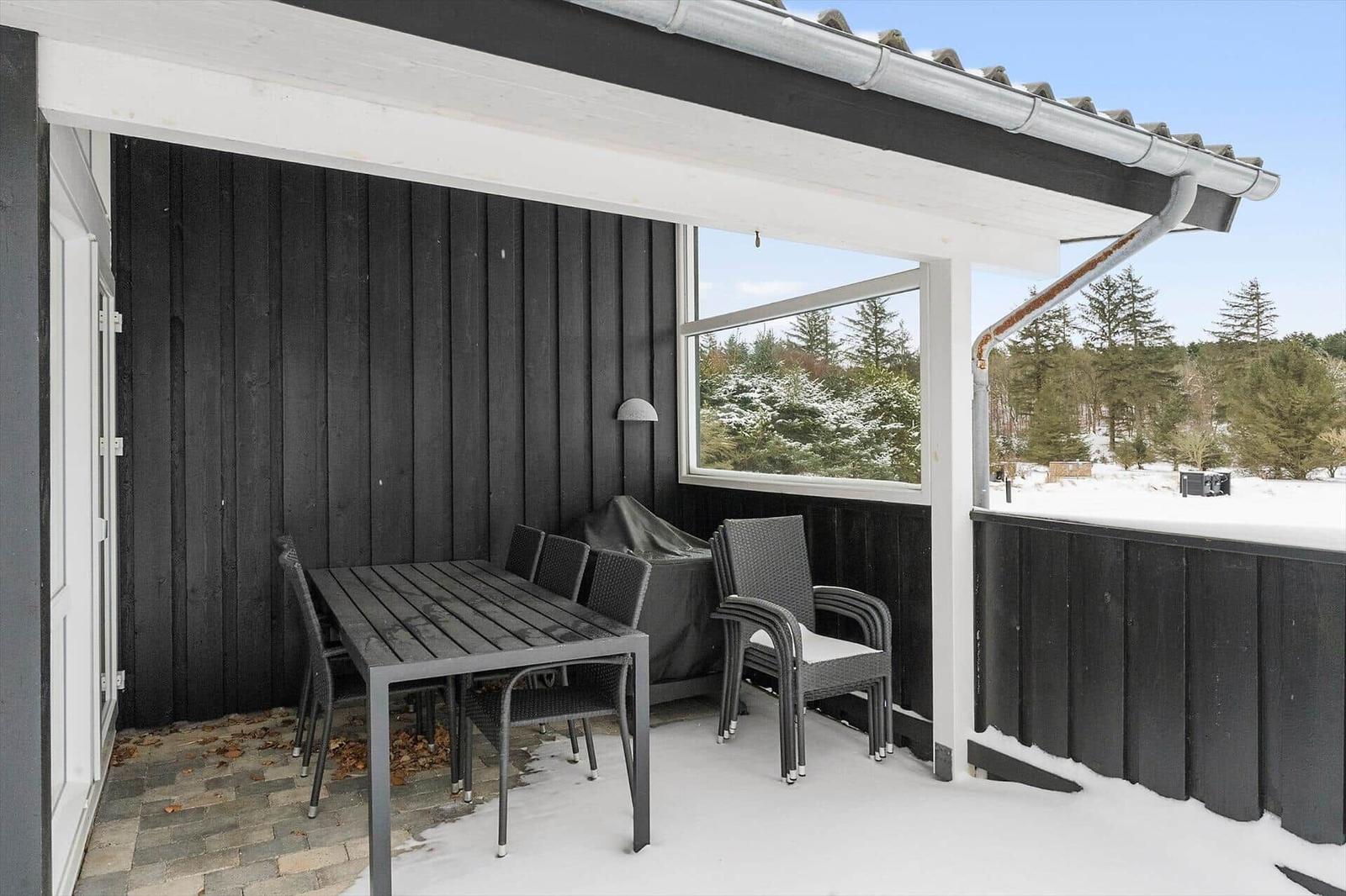 Patio with table, chairs, and grill under roof. Snow covers the ground and surrounding trees.
