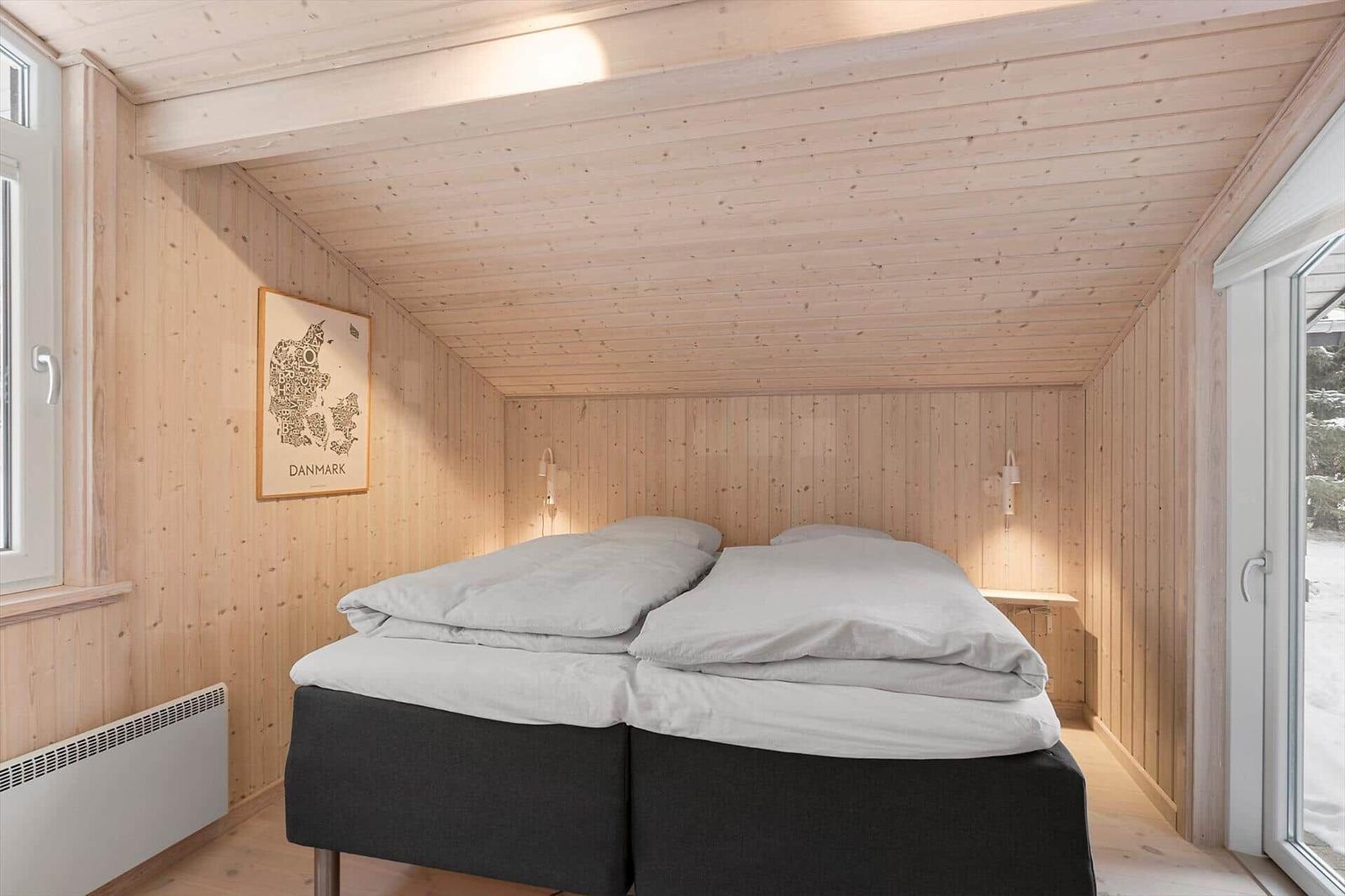Bedroom with double bed, wooden walls, and windows. Wall art with map of Denmark.