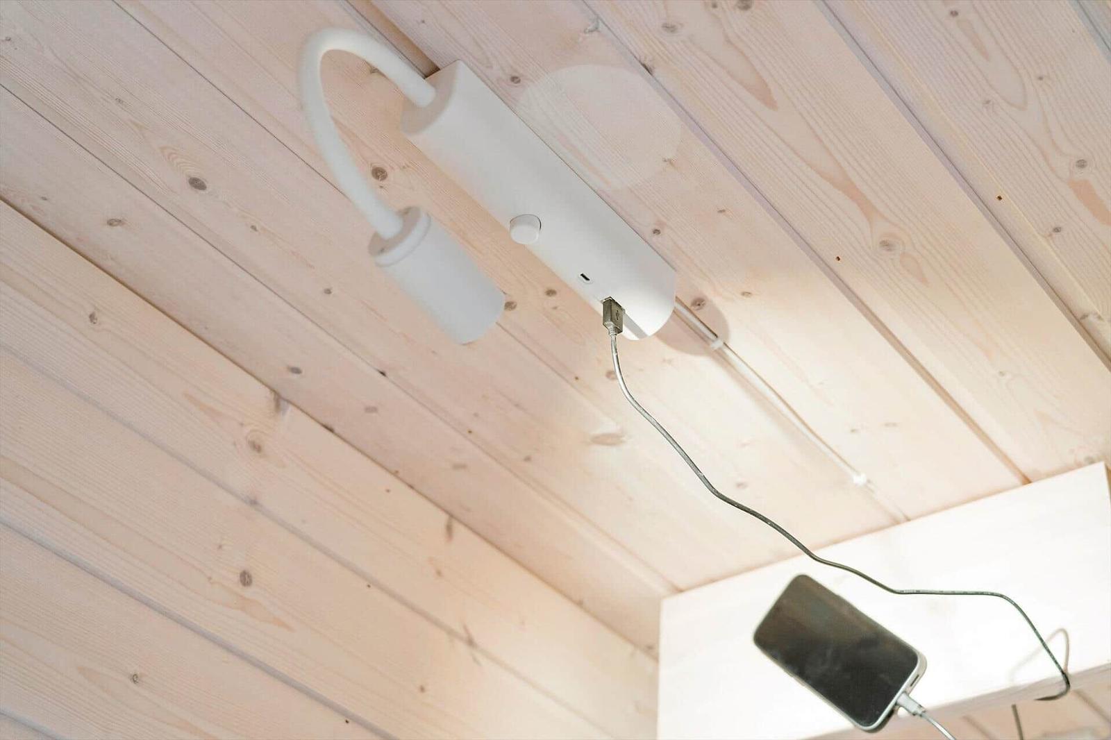 A white ceiling lamp with USB port charges a smartphone.