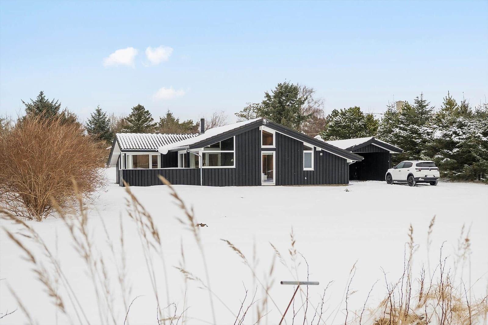Black house with snow, white car, and trees in the background.