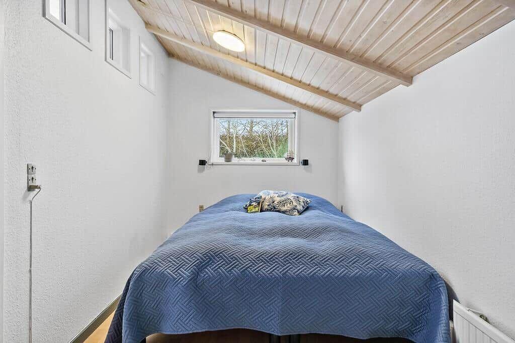 Bedroom with blue quilt and wooden ceiling.
