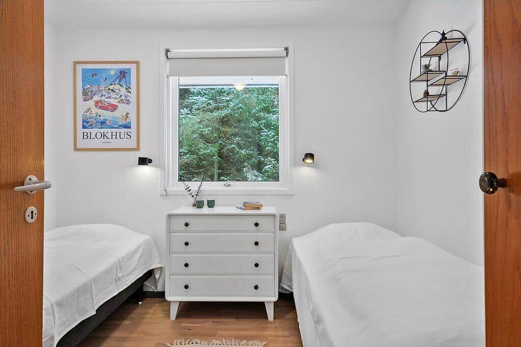 Two beds, dresser, and window with view of forest.