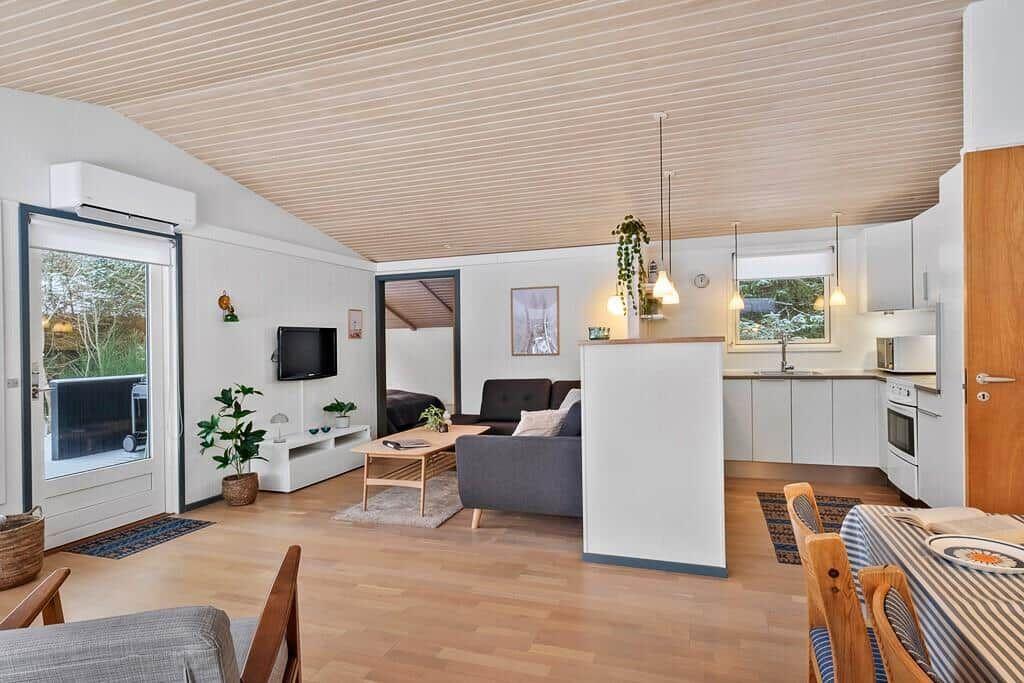 Apartment with open kitchen, sofa and TV. Wooden floor and sloped ceiling.