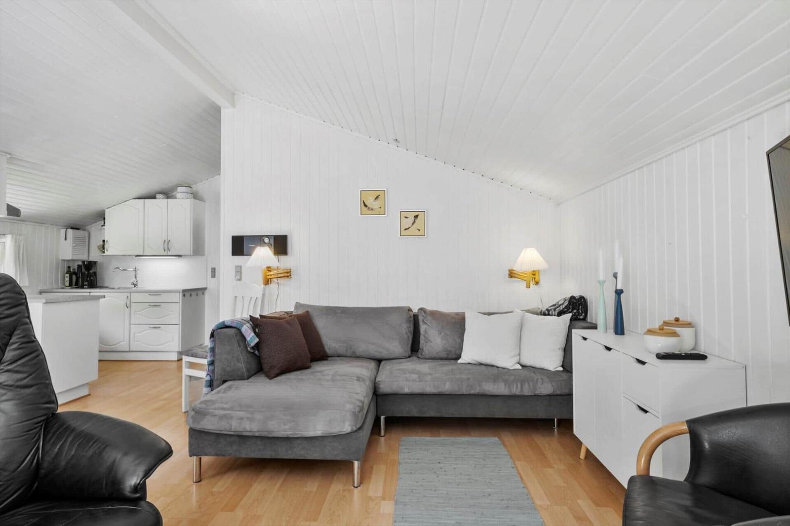 Living and kitchen area with gray sofa, white walls, and wooden floor.
