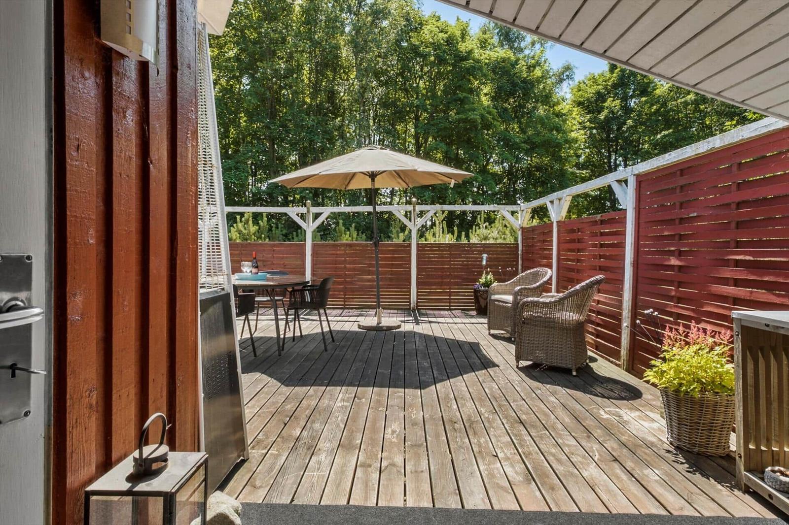 Deck with table, chairs, and umbrella. Red wooden fence and plants.