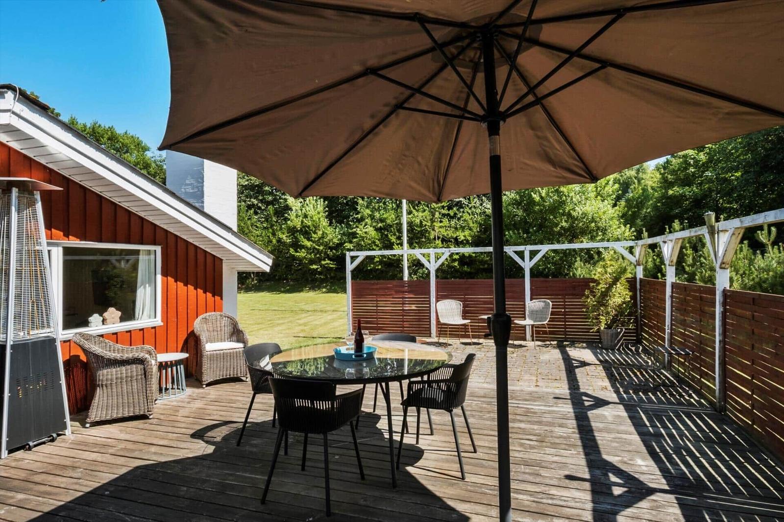 Deck with table, chairs, and umbrella beside red house.