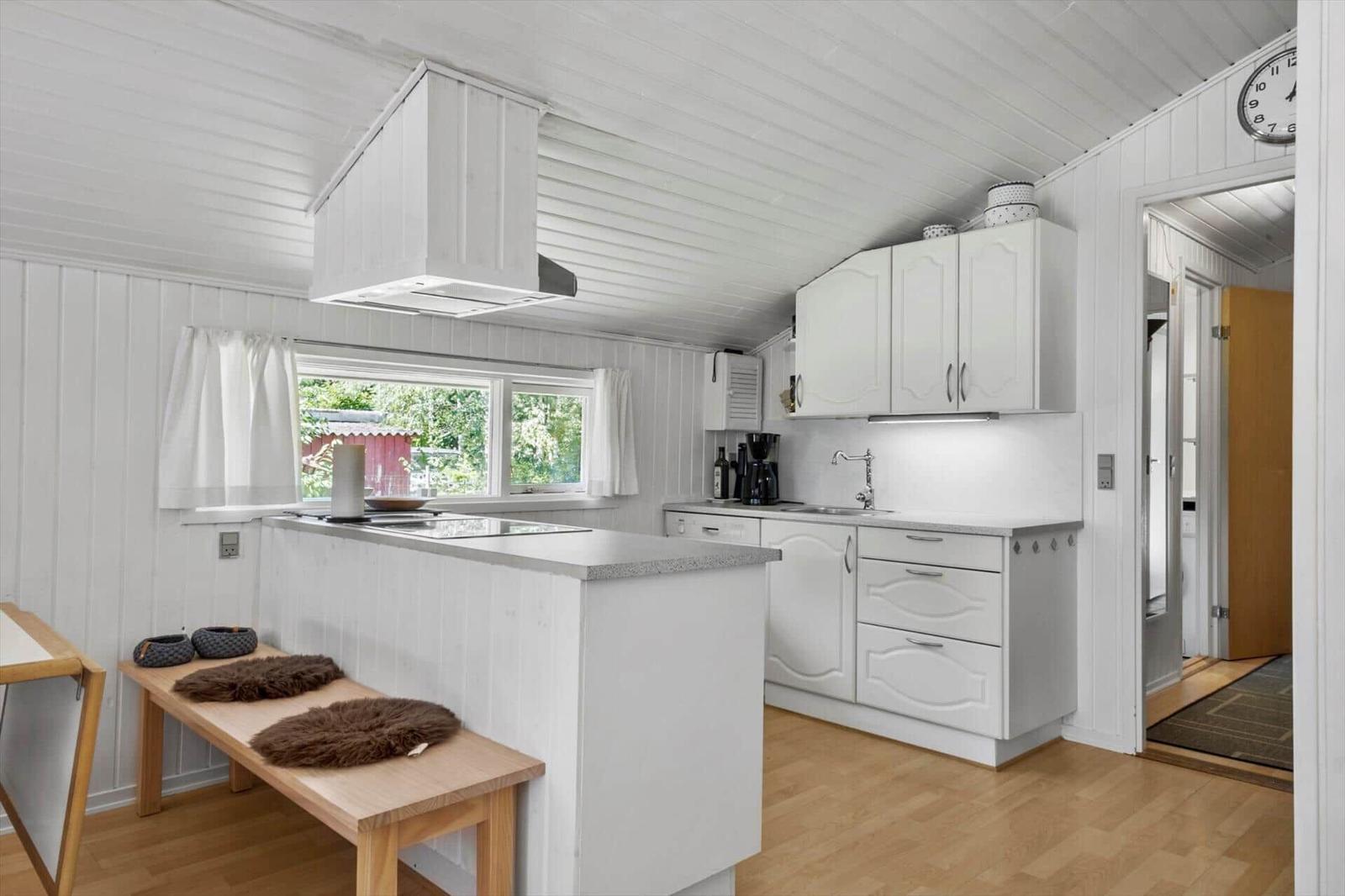 Kitchen with white cabinets and wooden floor. Window with view of garden.