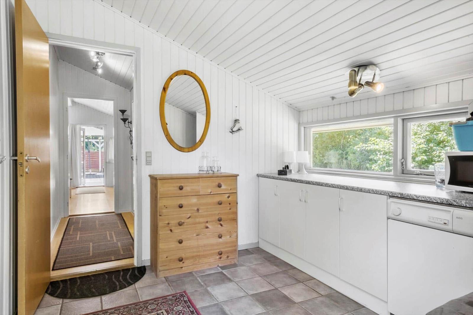 Kitchen with white cabinets and wooden dresser. Hallway leading to garden view.