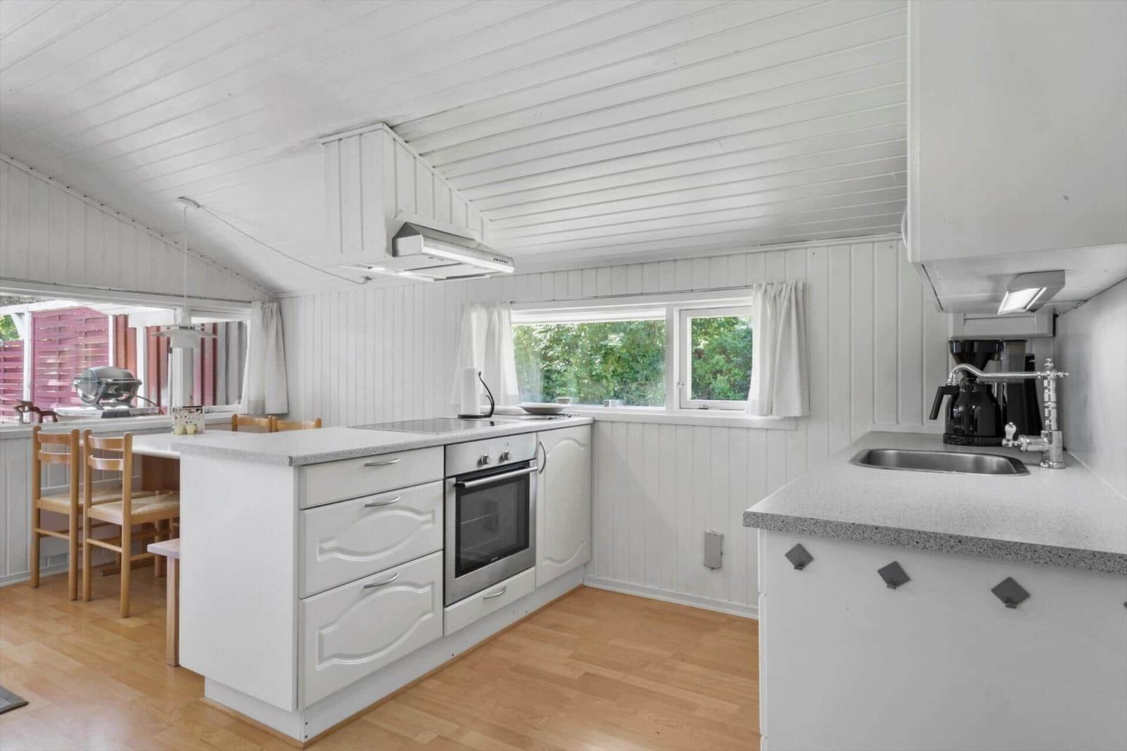 Kitchen with white cabinets, wooden floor, and windows overlooking greenery.
