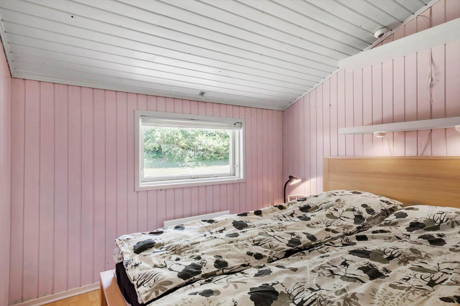 Bedroom with pink paneled walls, bed, and window.