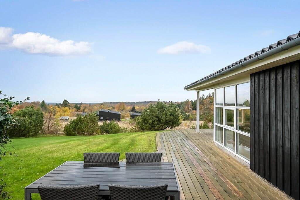 Deck with table and chairs, view of green lawn and forest.