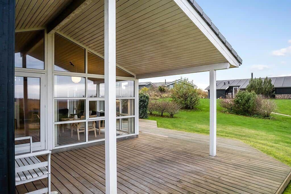 Deck with wooden flooring and glass walls. View of green lawn and trees.
