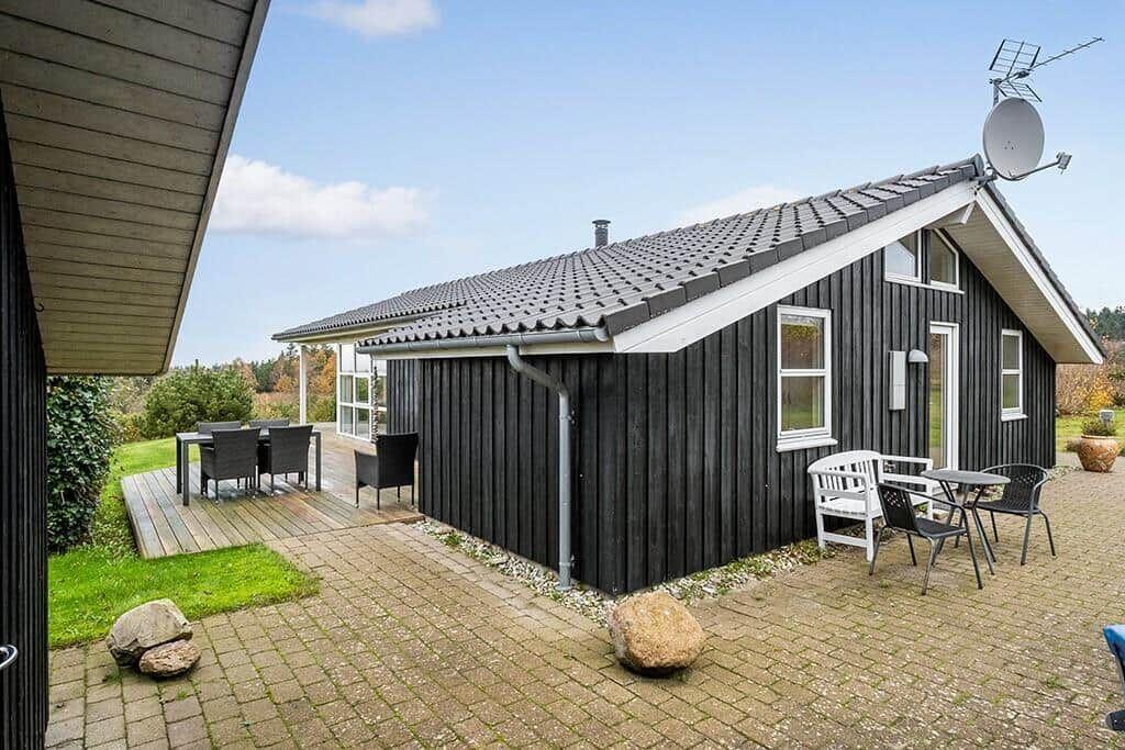 Black wooden house with terrace, garden, and seating areas.