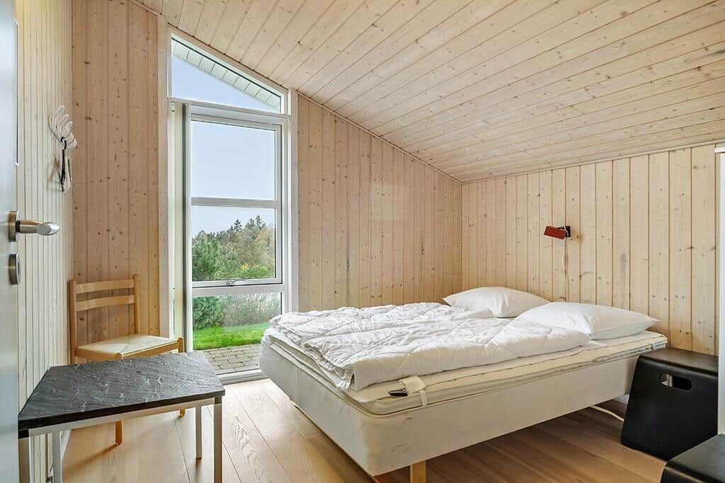 Bedroom with wooden walls and large window to greenery.