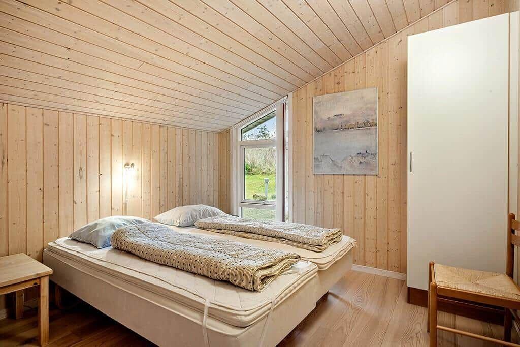 Bedroom with wooden walls, bed, window, and wardrobe.