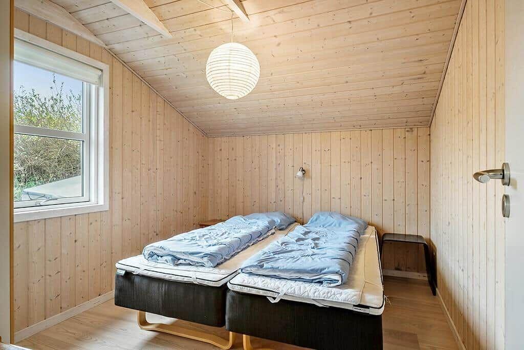 Room with two mattresses, wood walls and window. Ceiling with lamp.
