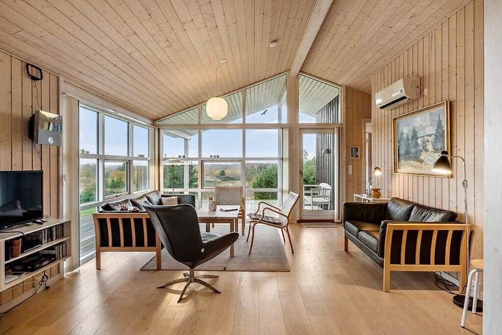 Living room with wooden walls, large windows, and dark sofas.