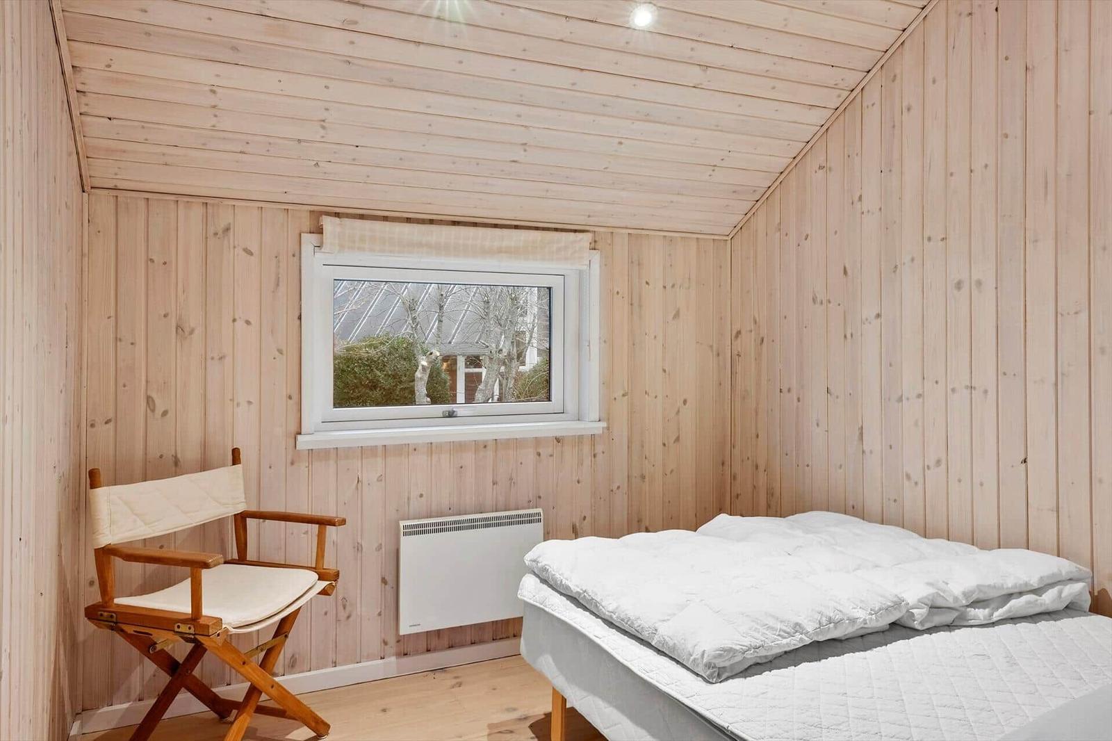 Schlafzimmer mit Bett, Stuhl und Fenster. Holzwände und Decke.