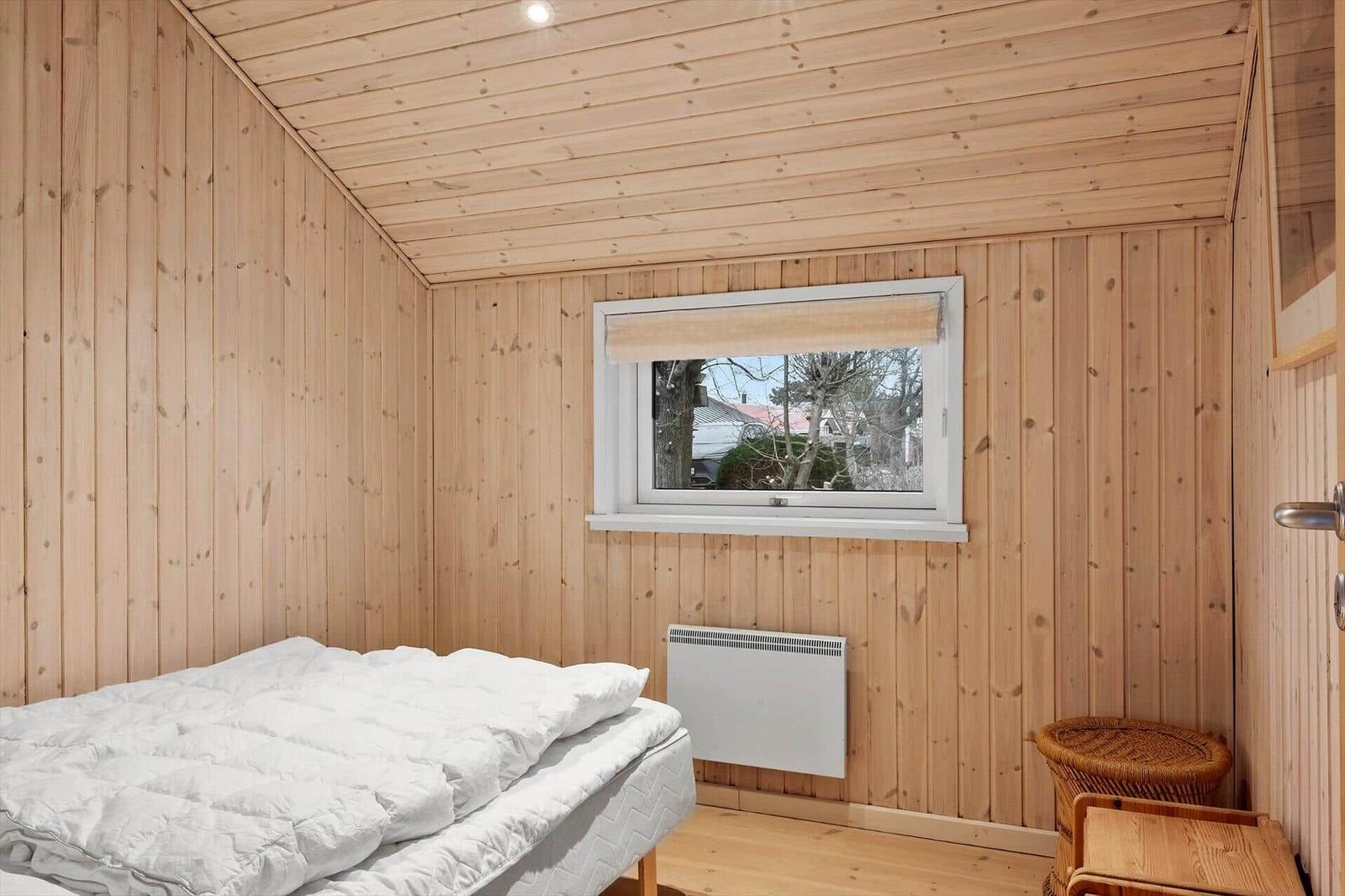 Schlafzimmer mit Holzwand, Bett, Fenster und Heizkörper.