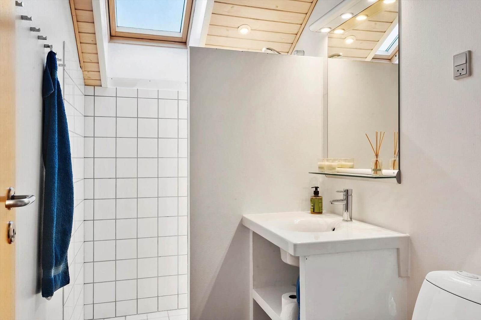 Badezimmer mit Dusche, Waschbecken und Toilette unter Holzdecke mit Dachfenster.