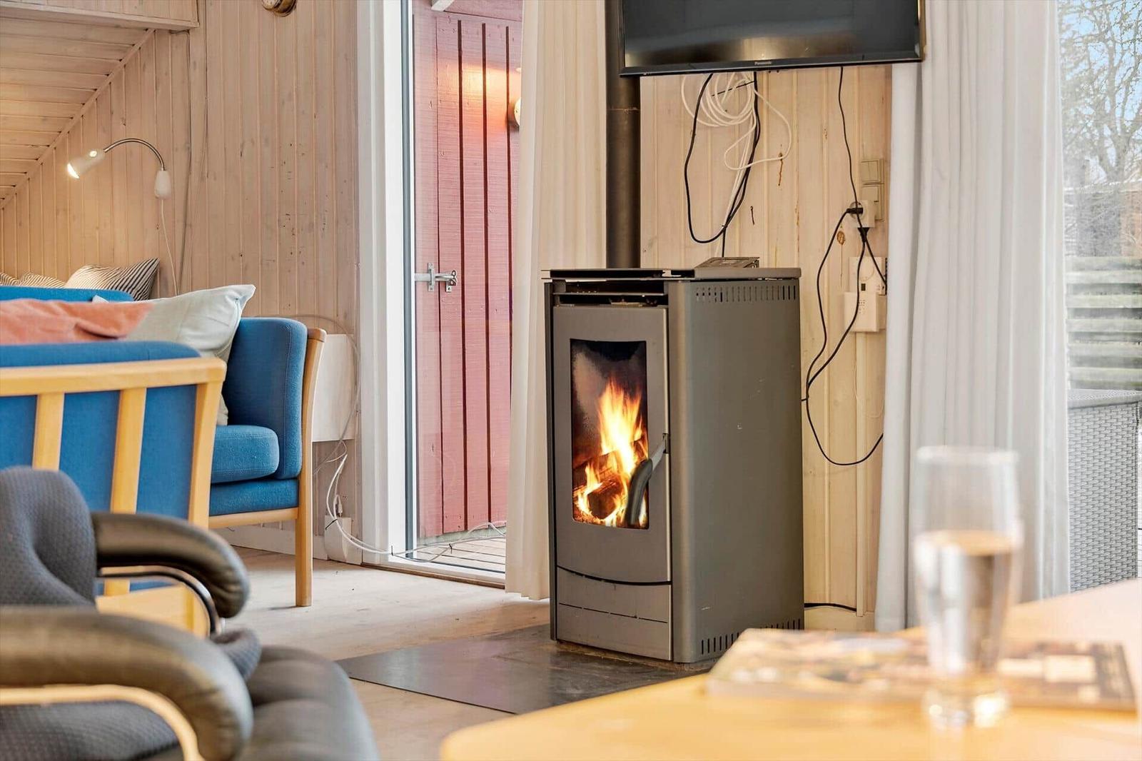 Kaminofen mit brennendem Feuer in einem Raum mit Holzwänden und blauer Couch.