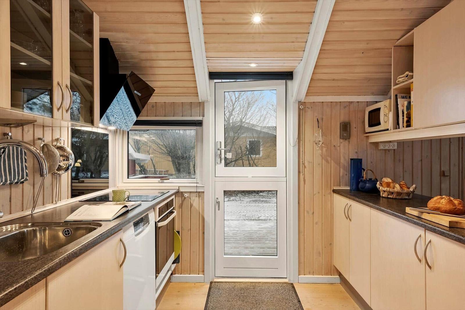 Küche mit Holzwänden, Arbeitsplatte und Tür zum Außenbereich.