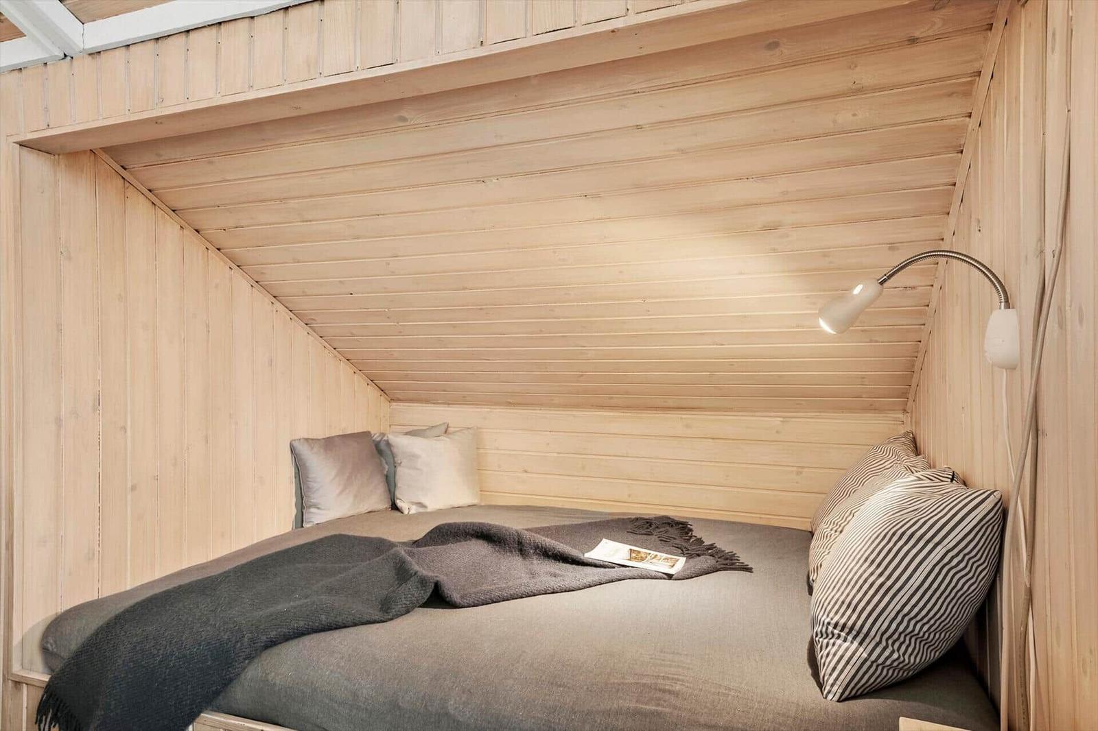 Ein Bett mit Kissen und Decke in einem holzverkleideten Raum mit schräger Decke.