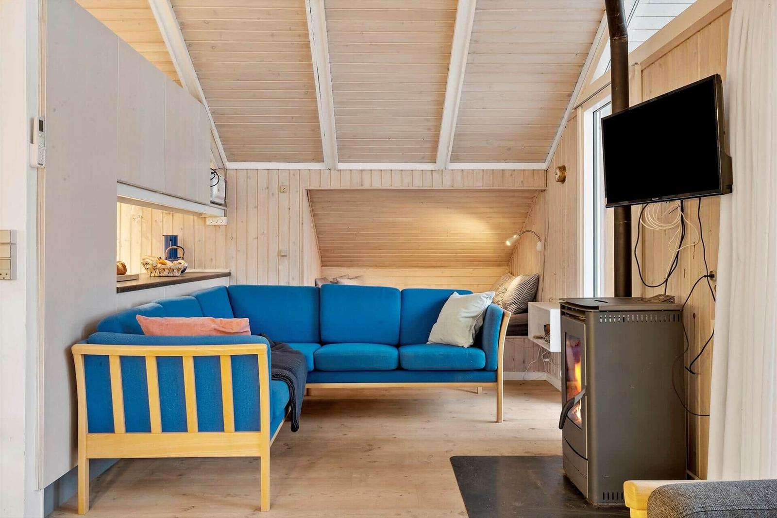 Wohnbereich mit blauem Sofa, Kamin und TV. Holzwände und -decke.