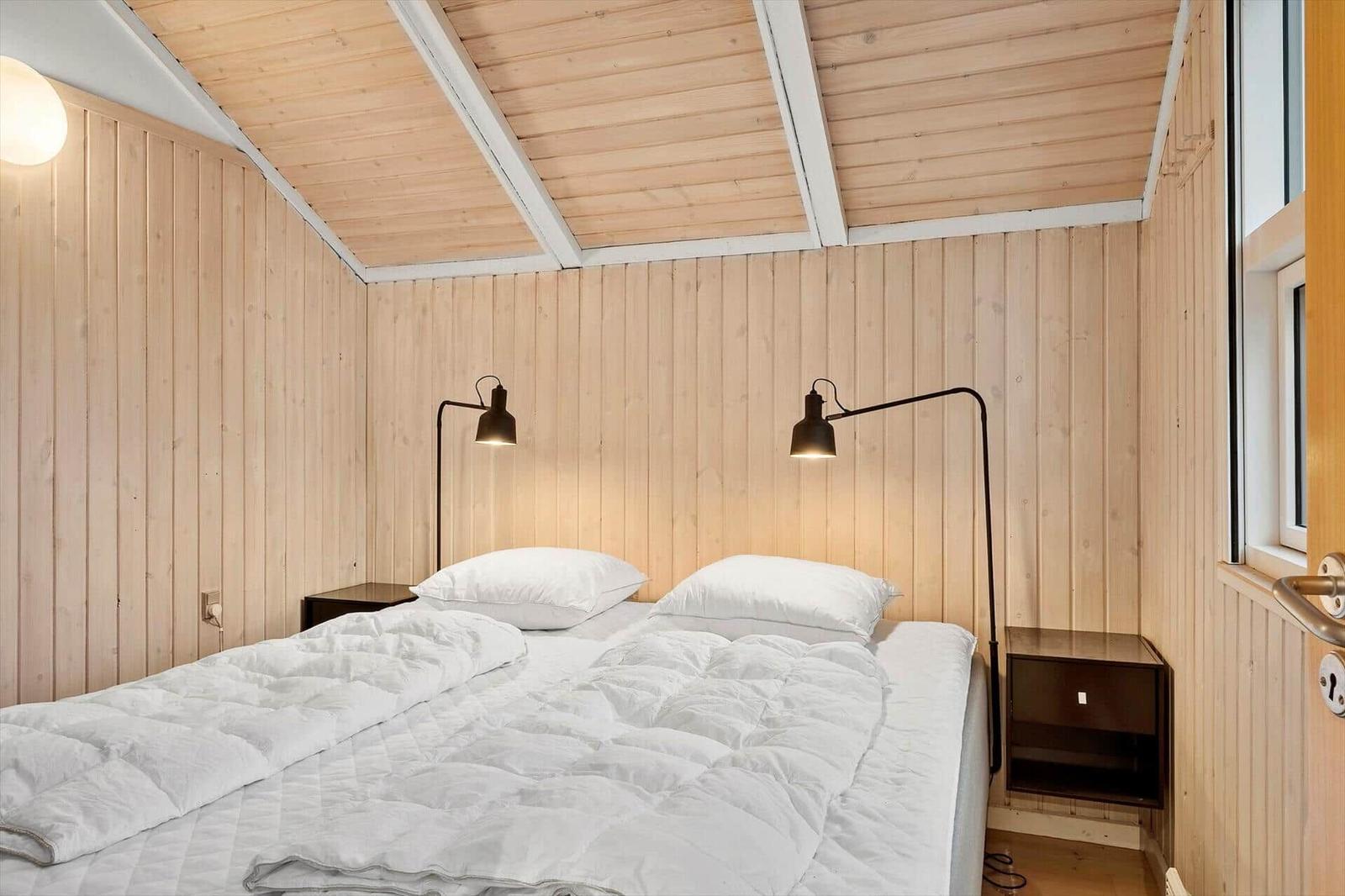 Schlafzimmer mit Holzwand und Bett mit weißen Kissen.