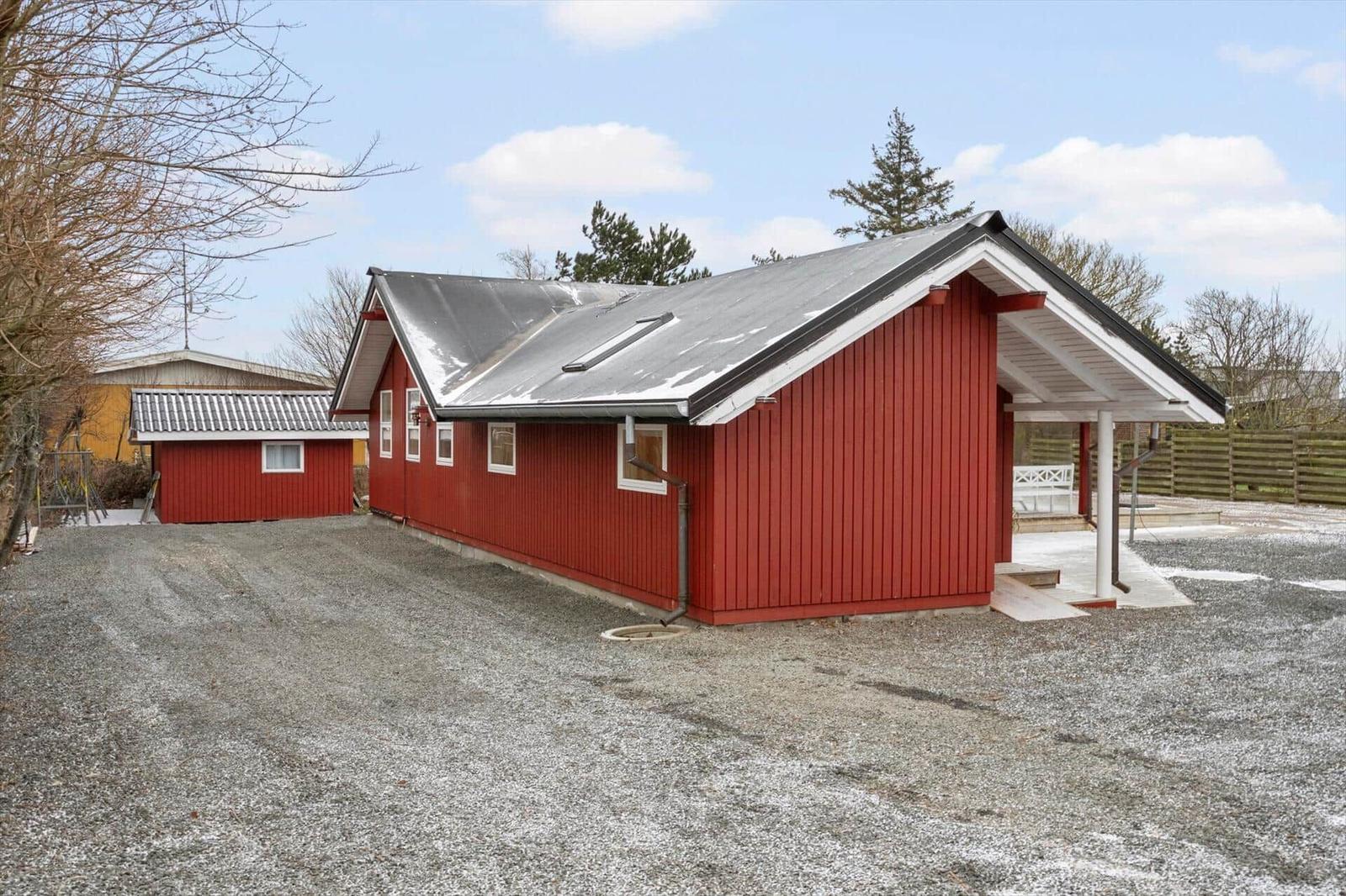 Rotes Holzhaus mit grauem Dach und Veranda auf Kiesfläche.