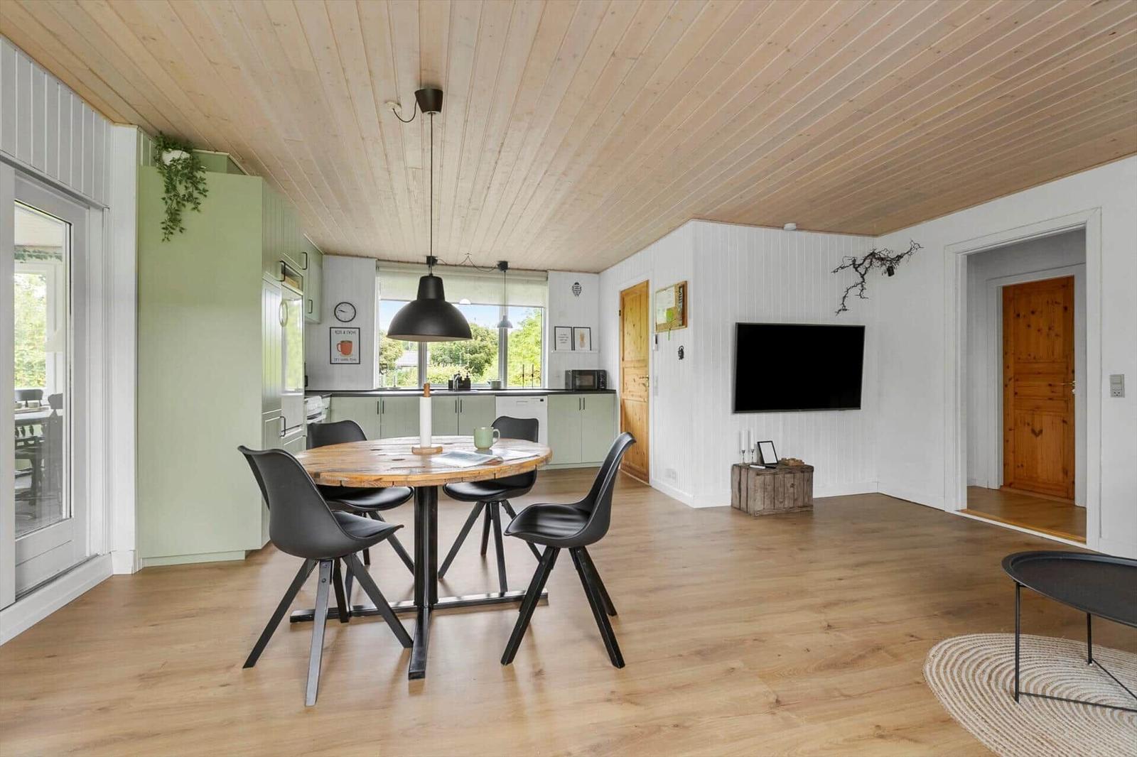 Open space with dining table, kitchen, and TV mounted on the wall.