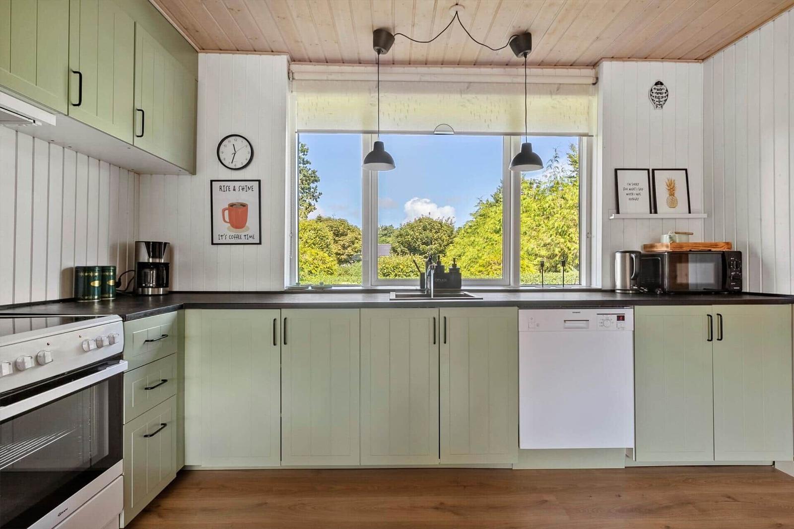 Kitchen with green cabinets, window with view of greenery, sink and dishwasher.