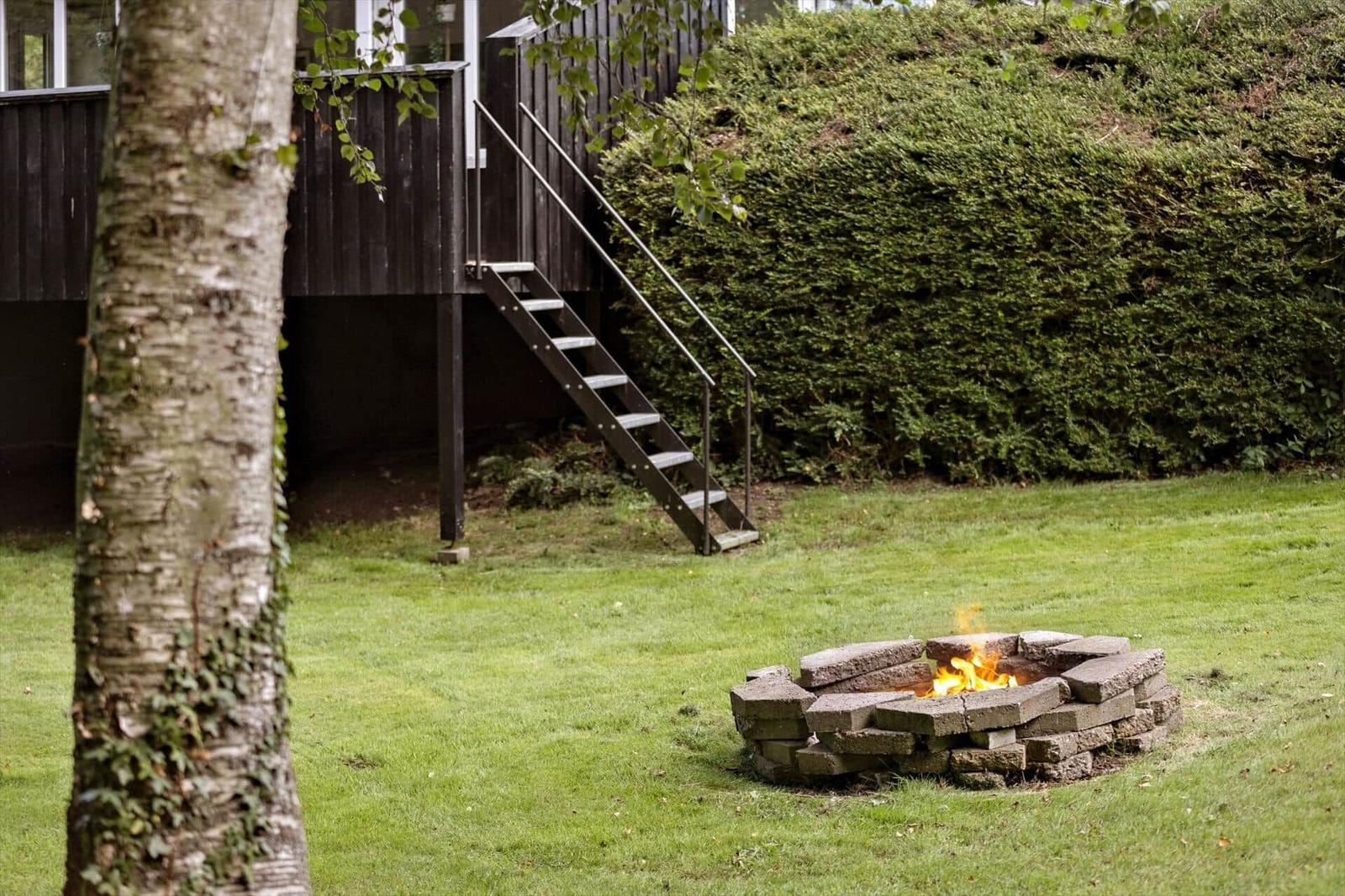 Fire pit in the garden in front of a house with wooden terrace and stairs.