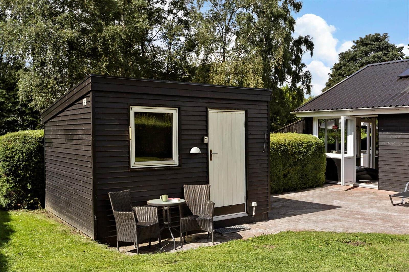 Wooden house with terrace, table, and chairs. Surrounded by greenery and sky.