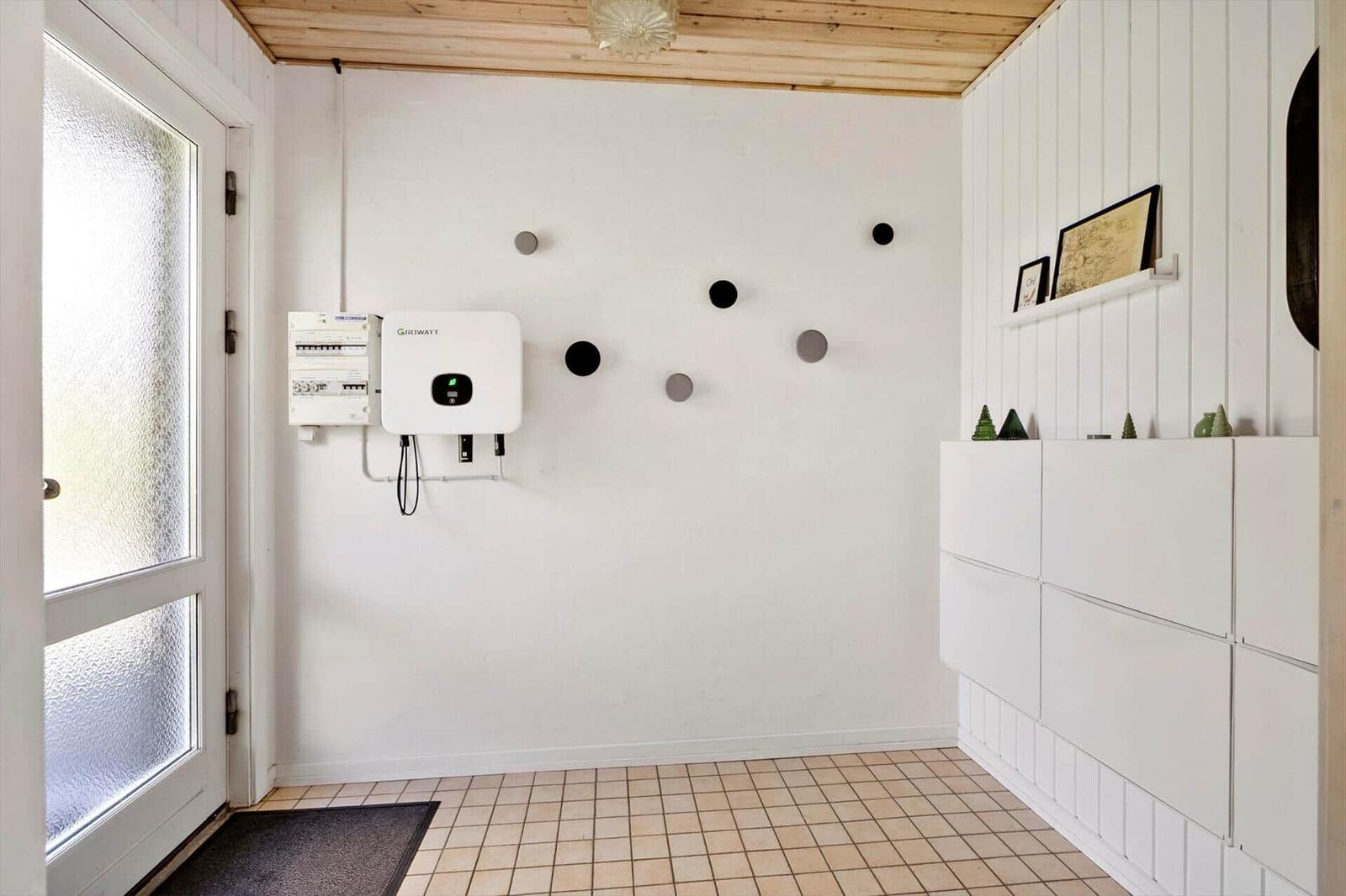Entrance area with white wall, wooden ceiling, and tiled floor. A power storage unit is mounted on the wall.