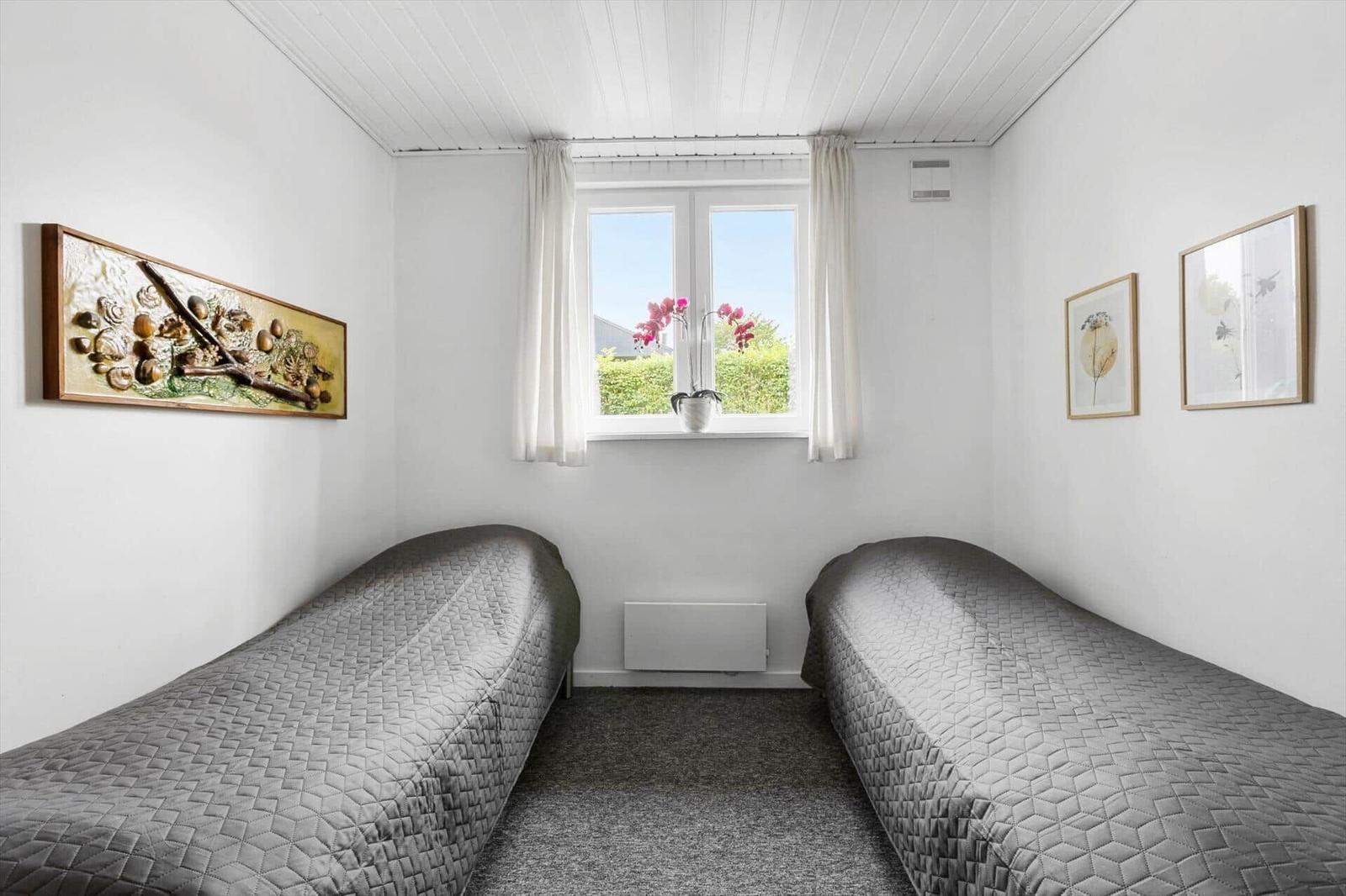 Two beds with gray bedding, window with white curtains and wall decor.