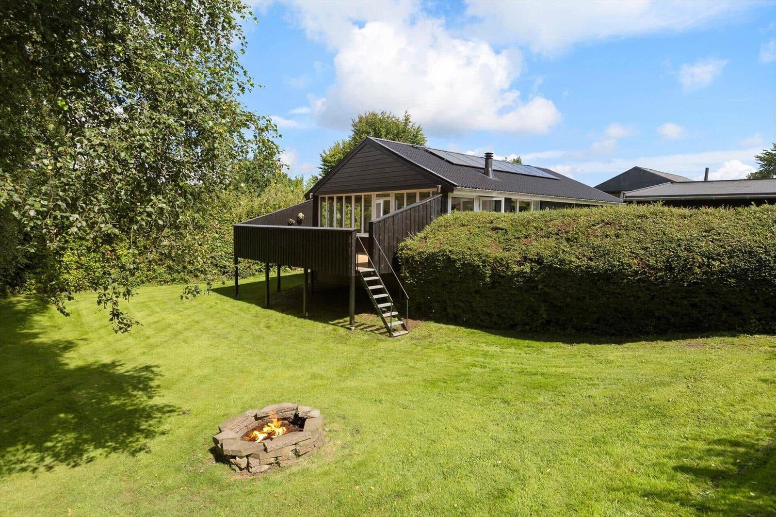 House with terrace, fire pit, and lawn under blue sky.