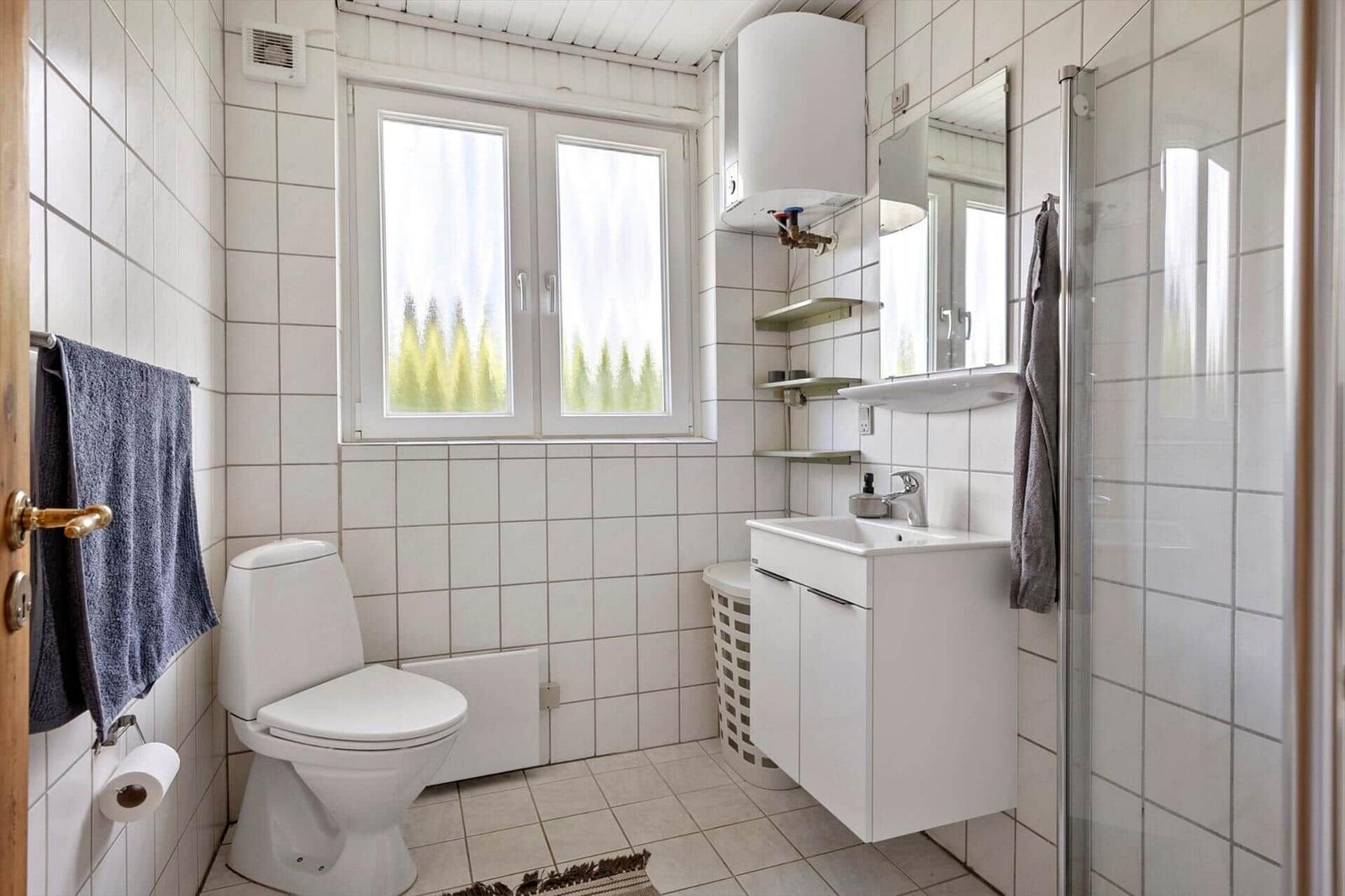 Bathroom with toilet, sink, and shower. Window with view of trees.