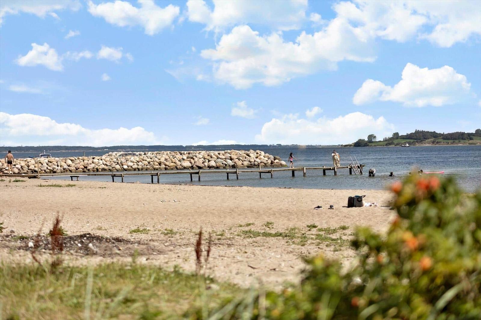 Beach with rock breakwater and wooden pier. People swim and enjoy the view.