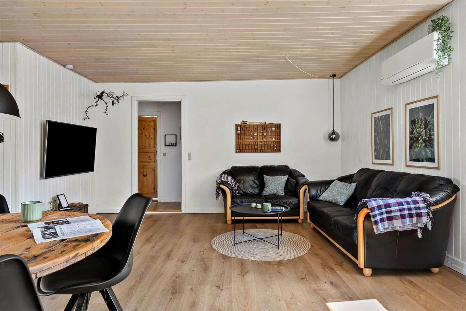 Living and dining area with wooden floor, black sofas, and TV mounted on the wall.