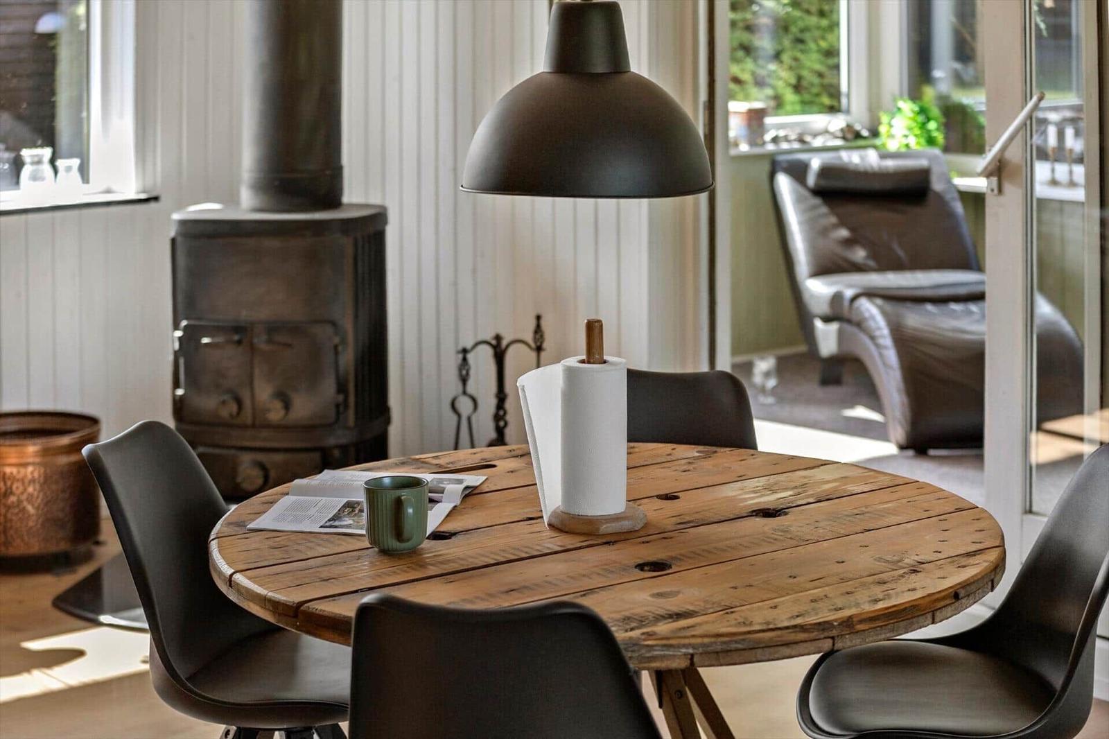 Round wooden table with chairs, coffee mug, and paper towel holder. Background: stove and seating area.