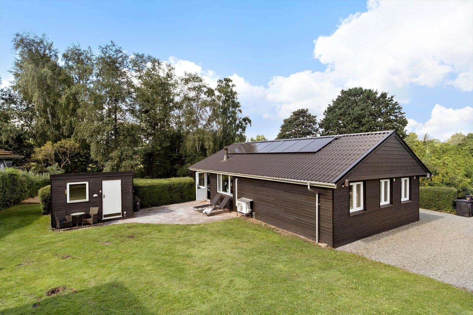 Wooden house with solar panels and garden. Outdoor terrace with sun loungers.