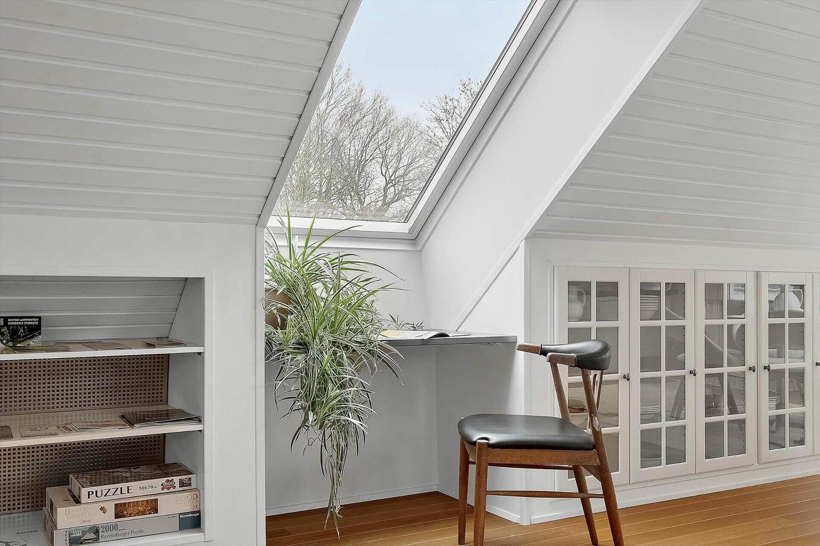 Dachgeschosszimmer mit Dachfenster, Pflanze, Stuhl und Glasfrontschrank.