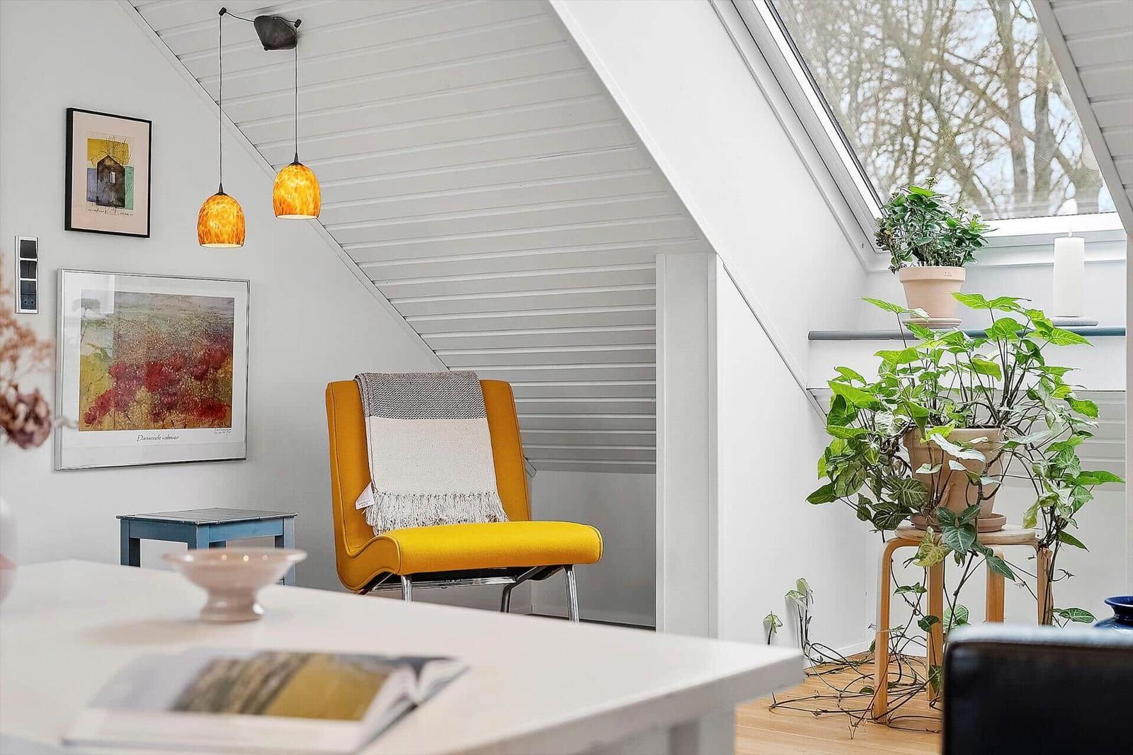 Ein Raum mit gelber Sessel, Pflanzen und Bildern an der Wand.