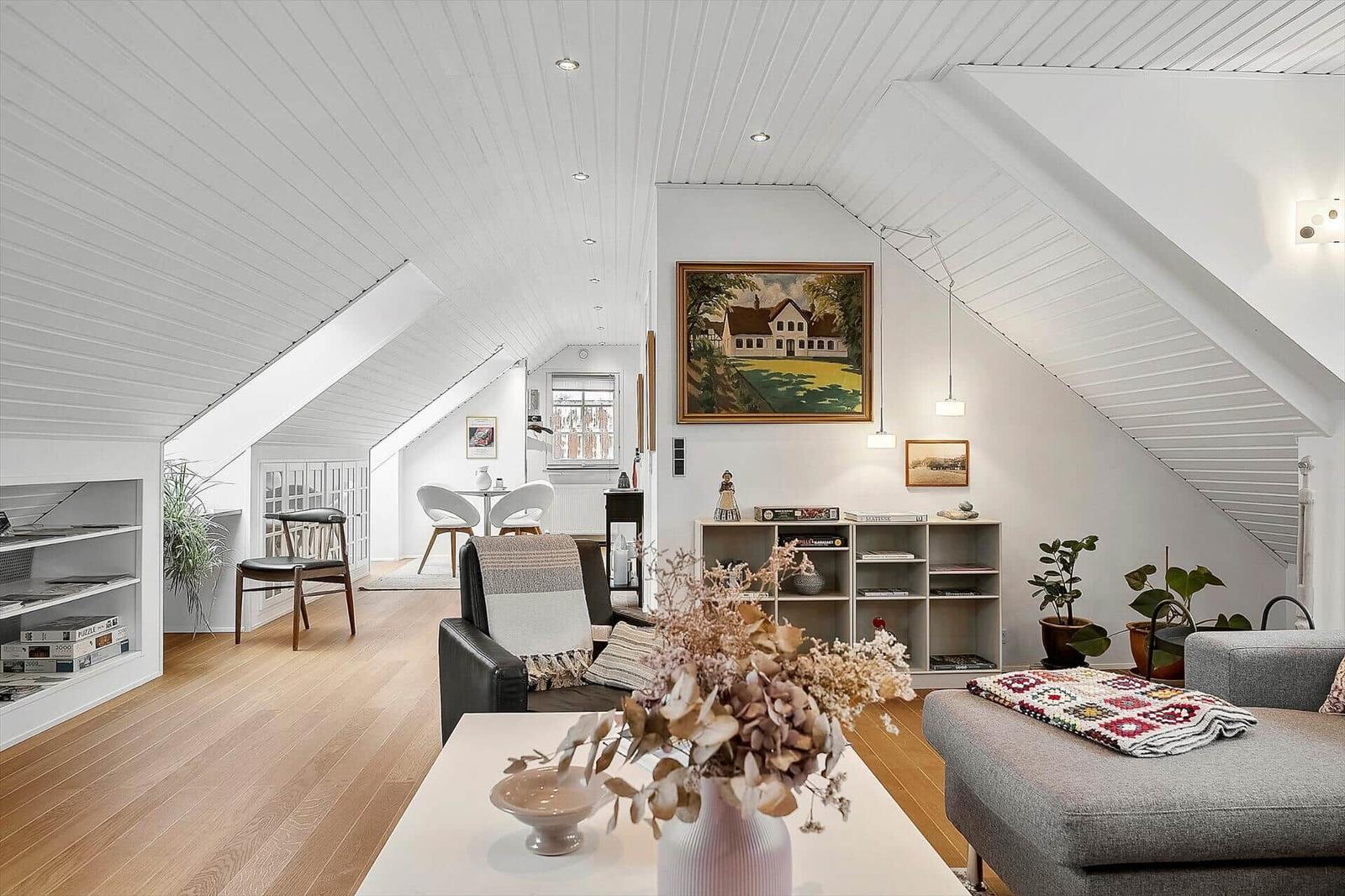 Wohnzimmer mit Dachschrägen, Holzboden und Möbeln. Wandbild und Pflanzen sichtbar.