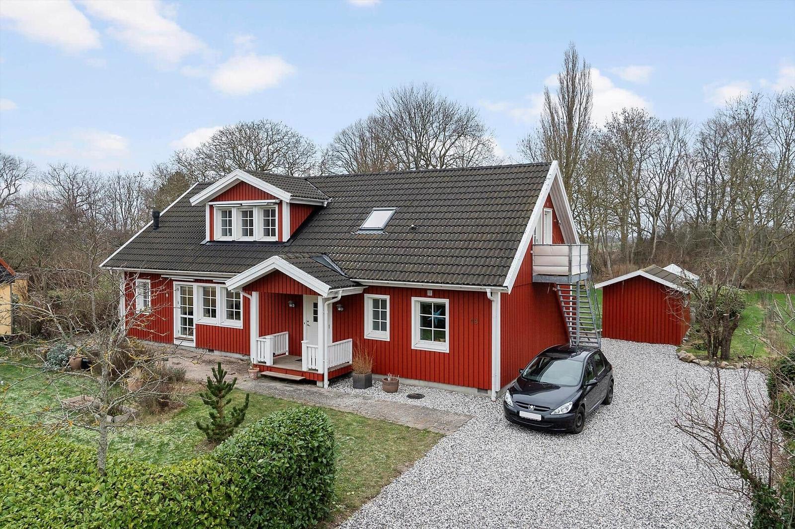 Rotes Holzhaus mit weißem Kranz, Garage und gepflastertem Hof.