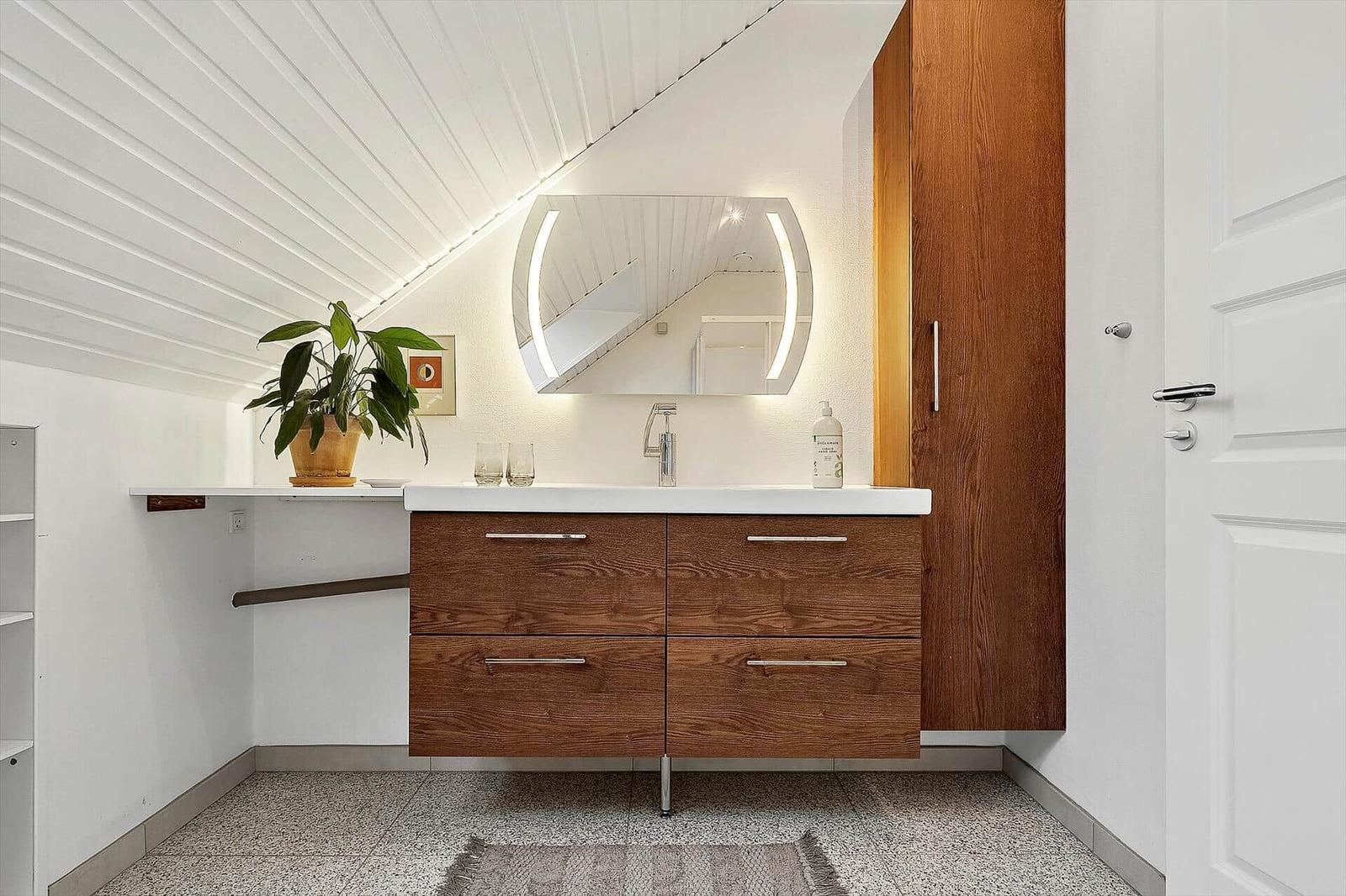 Badezimmer mit Holzschrank, Waschbecken und Spiegel unter schrägem Dach