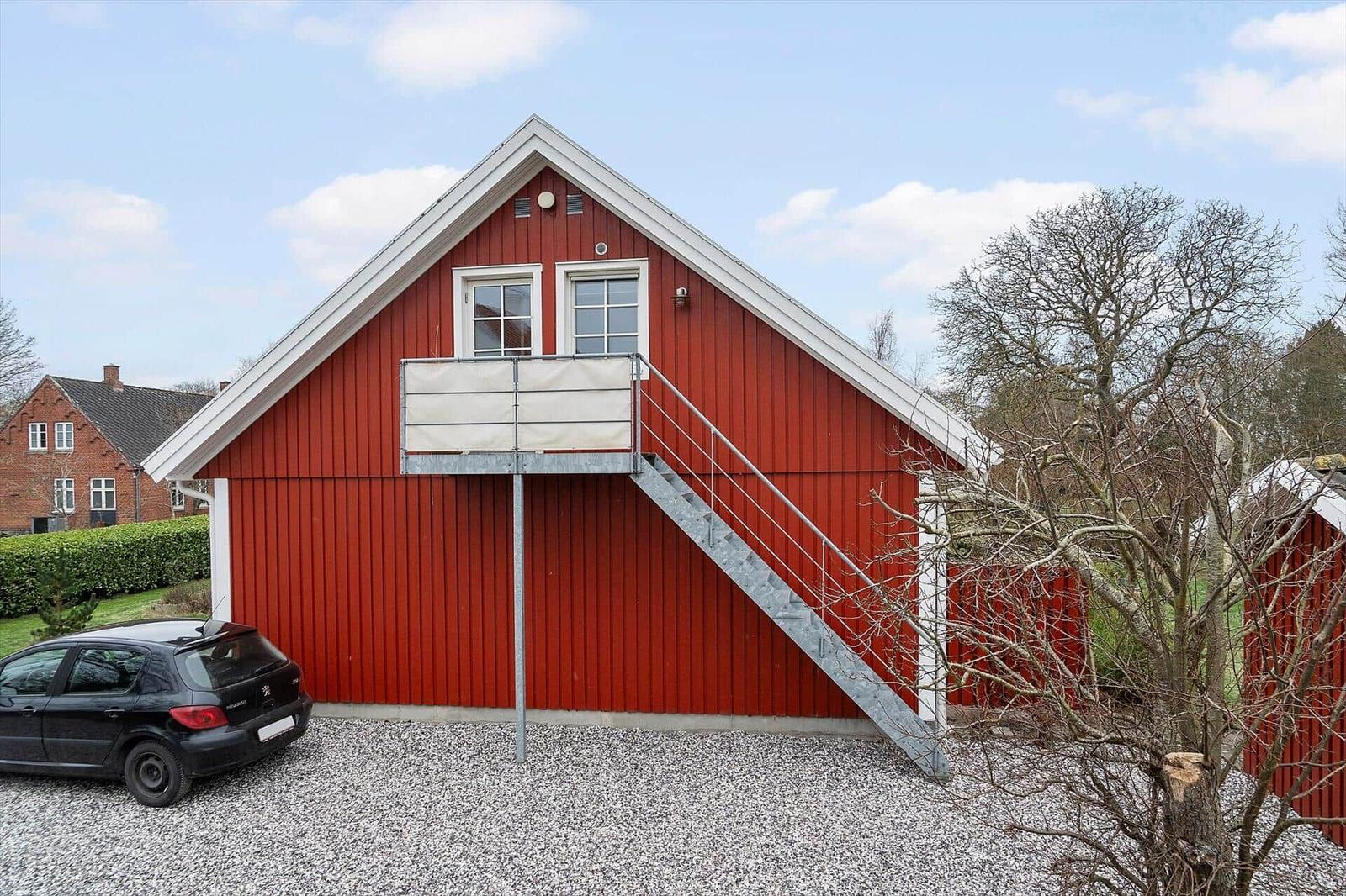 Rotes Holzhaus mit Balkon und Treppe. Auto parkiert auf Kies.